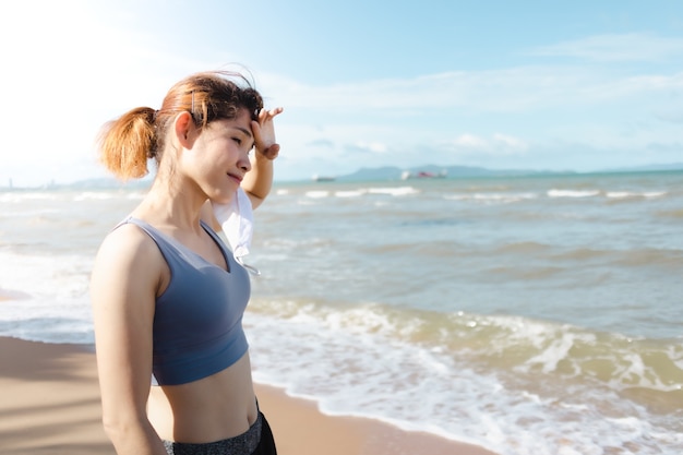 Mulher tira a máscara e descansa após terminar de correr na praia no verão