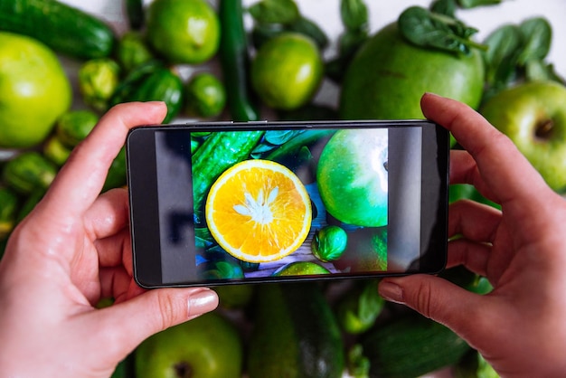 Mulher tira foto no telefone de frutas verdes com laranja no meio