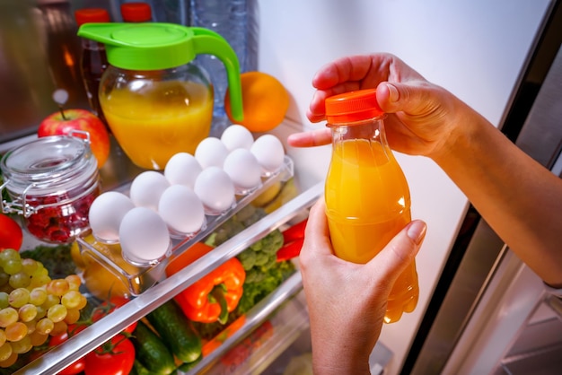 Mulher tira o suco de laranja da geladeira aberta