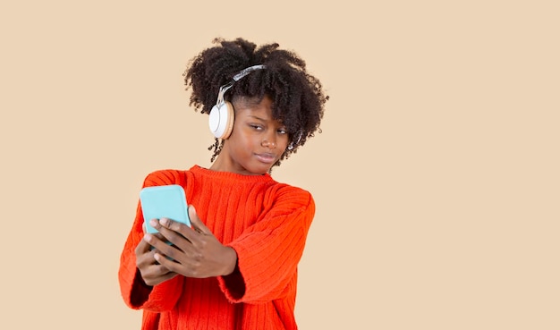 Mulher tirando selfie com o celular enquanto ouve música com fones de ouvido sobre fundo claro