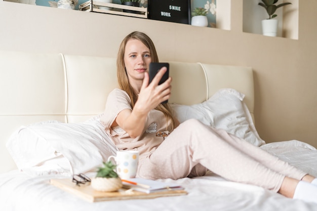 Mulher tirando uma selfie no smartphone enquanto está sentada na cama