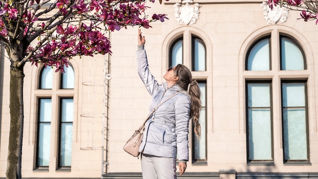 Mulher tocando árvore com flores cor de rosa. Antigo palácio feito em estilo europeu clássico ao fundo