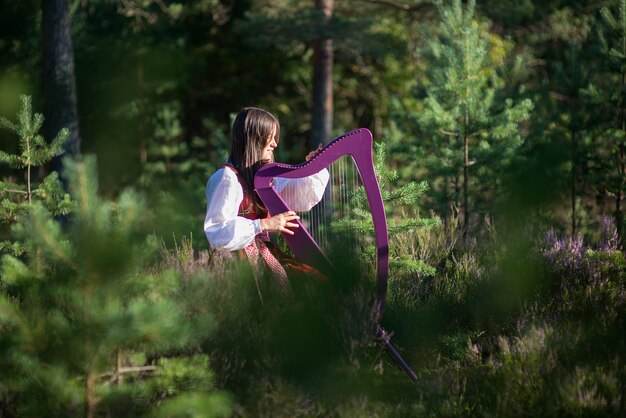 Mulher tocando harpa contra árvores na floresta