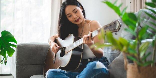 Mulher tocando instrumento de música de violão em casa jovem músico asiático estilo de vida