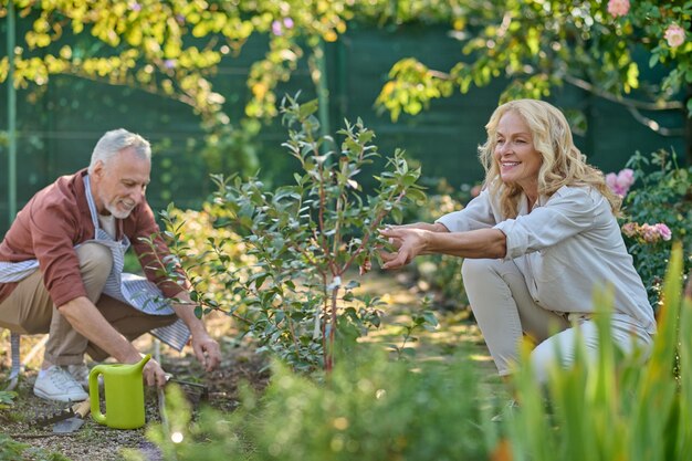 Mulher tocando planta homem pingando terra no jardim