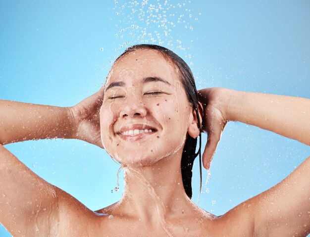 Mulher toma banho e sorri em cuidados com a pele para hidratação higiênica ou água contra um fundo de estúdio azul Modelo feminino feliz sorrindo de satisfação ou relaxando para lavagem de cabelo saudável e limpa ou cosméticos