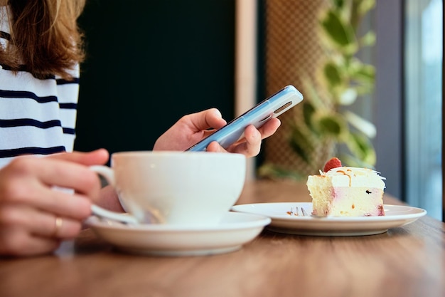 Mulher toma café da manhã no café usa smartphone no café