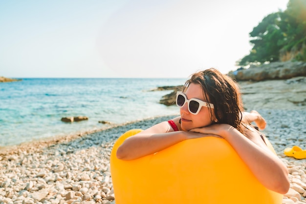 Mulher tomando banho de sol na praia do mar, deitada no espaço de cópia do sofá de ar amarelo