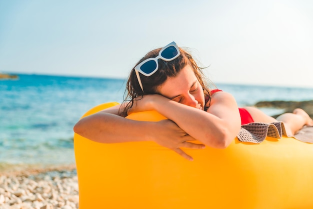 Mulher tomando banho de sol na praia do mar deitada no sofá de ar amarelo