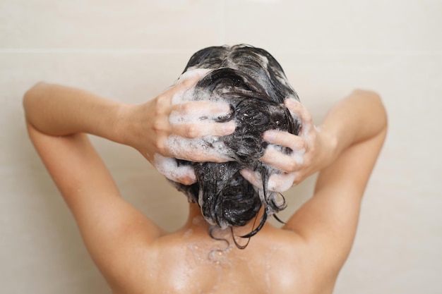 Mulher tomando banho e lavando o cabelo com xampu no banheiro em casa