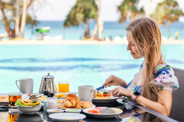 Mulher tomando café da manhã americano com bule na mesa ao lado da piscina no resort