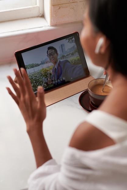 Mulher tomando café da manhã ao fazer videochamada para seu colega de trabalho de outro país