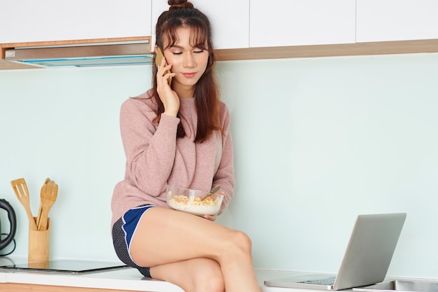 Mulher tomando café da manhã e falando ao telefone