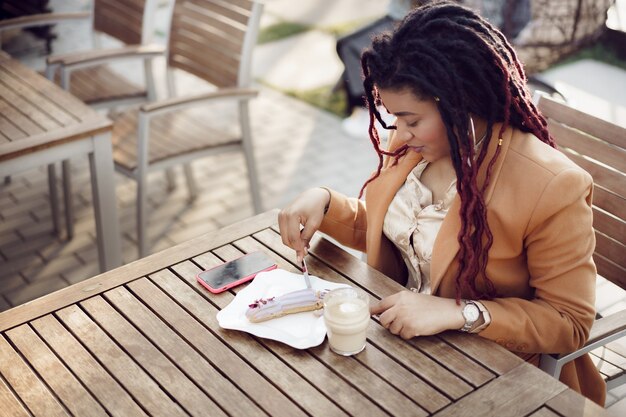 mulher tomando café e comendo sobremesa em uma cafeteria ao ar livre