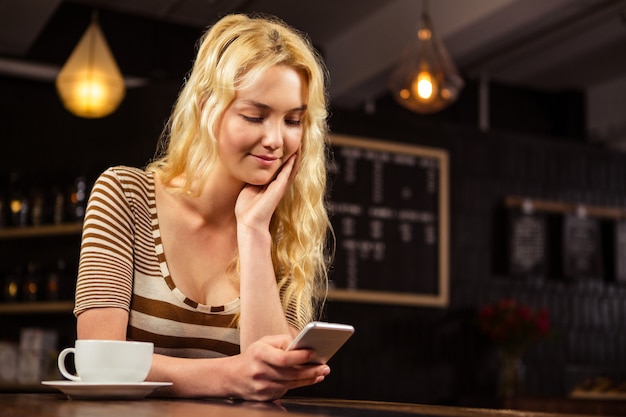 Mulher tomando café e usando smartphone