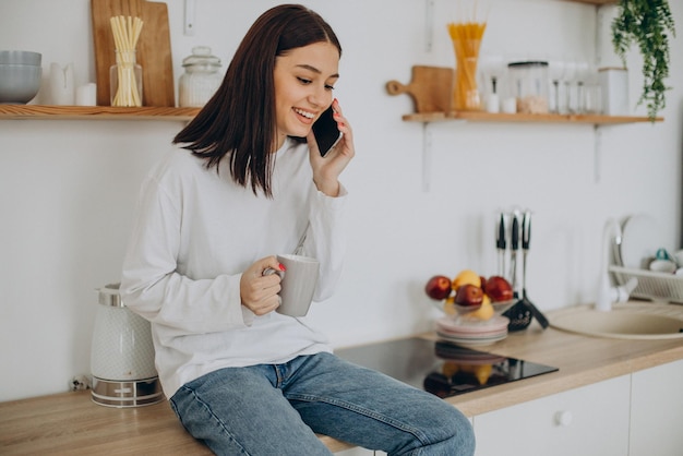 Mulher tomando café e usando telefone na cozinha