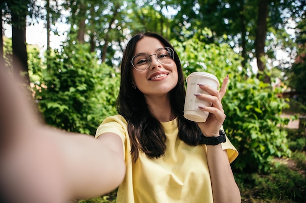 Mulher tomando café lá fora e tirando uma selfie