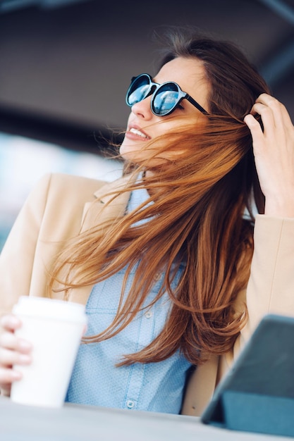 Mulher tomando café na rua e usando tablet