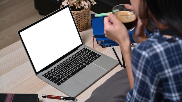 Mulher tomando café quente e usando laptop na sala de estar.