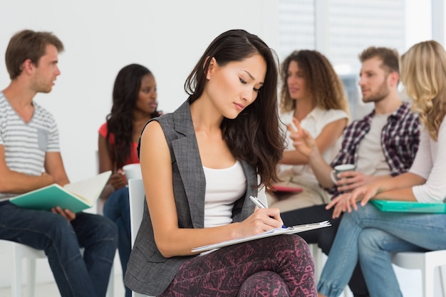 Mulher tomando notas enquanto os colegas estão falando atrás dela