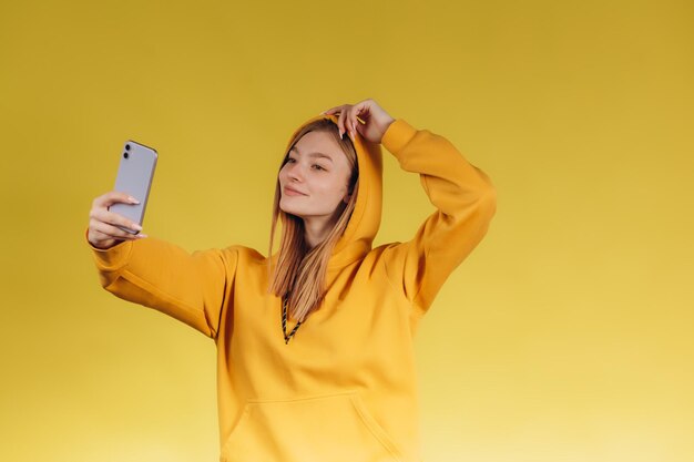 Mulher tomando selfie em fundo amarelo O adolescente está vestido com uma magrela amarela A garota está feliz