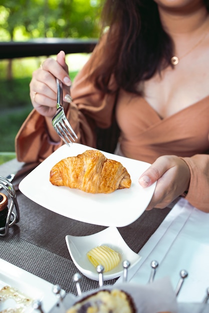 Mulher tomando um croissant no café da manhã