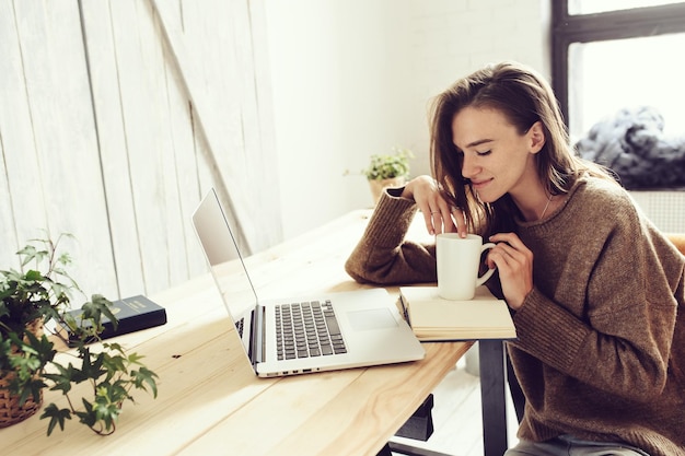 Mulher tomando uma bebida com laptop na mesa