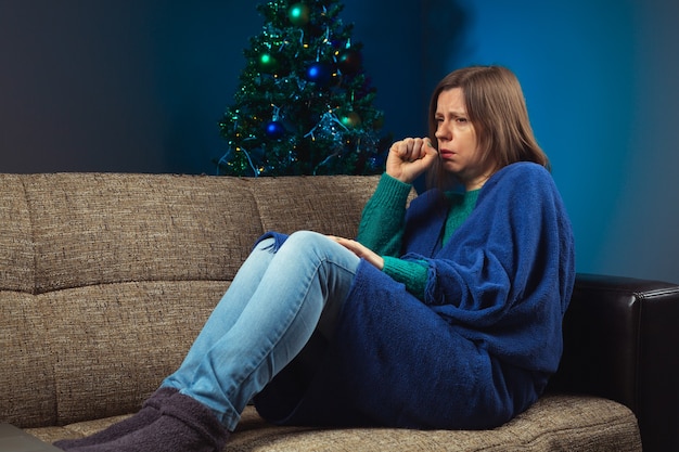 Mulher tossindo em um sofá com árvore de Natal decorada como comemorar quando você está doente