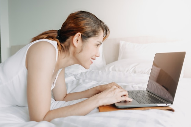 Mulher trabalha com laptop na cama conceito de trabalho do hotel