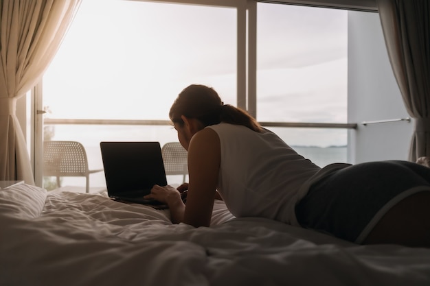 Mulher trabalha com laptop na cama conceito de trabalho do hotel