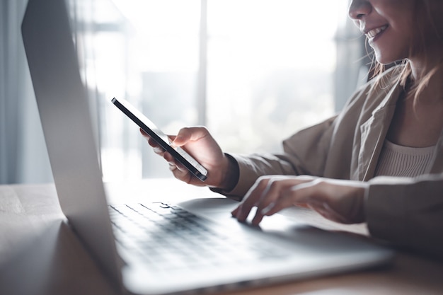 Mulher trabalha em casa e usando um smartphone e um laptop na mesa