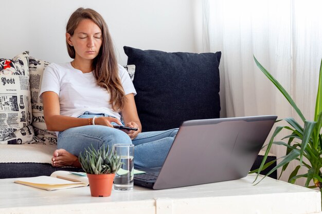 Mulher trabalha em casa, senta-se perto de um laptop com um notebook, um copo de água na mesa no espaço de trabalho doméstico