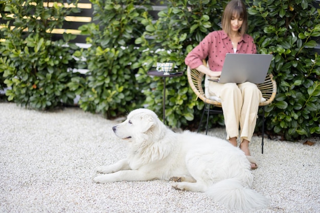 Mulher trabalha no laptop sentado com cachorro no jardim