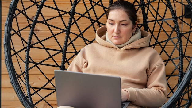 Mulher trabalha no laptop sentado na cadeira pendurada em casa