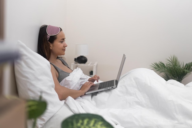 Mulher trabalha on-line e estuda remotamente enquanto envolvida em seu cobertor e usando seu laptop