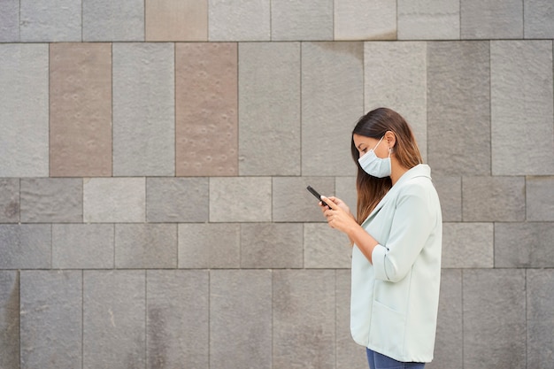 Mulher trabalhadora com máscara facial e usando smartphone. à esquerda, há um espaço vazio para integrar o texto.