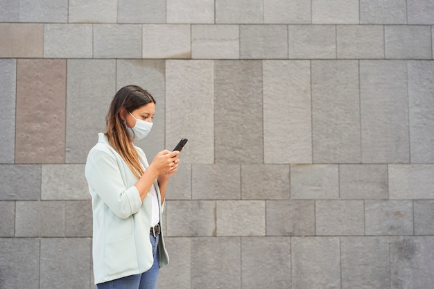 Mulher trabalhadora com máscara facial e usando smartphone