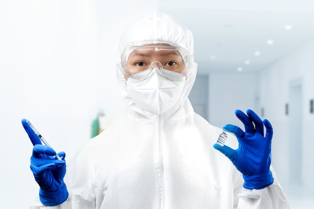 Mulher trabalhadora de saúde com um traje de proteção e luvas segurando covid 19 vacinas no hospital