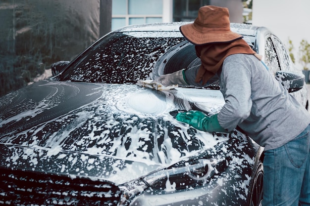 Foto mulher trabalhadora lavando carro na estação de carros ao ar livre com espuma e esponja amarela