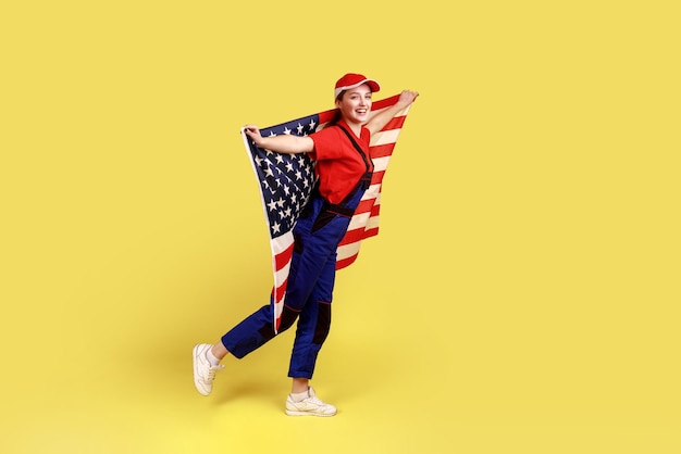 Mulher trabalhadora positiva feliz posando com bandeira americana nas mãos comemorando feriado patriótico