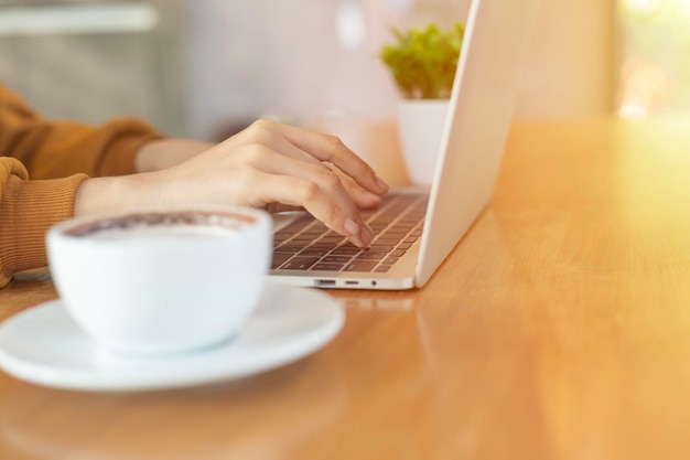 Mulher trabalhando com a mão e digitando no teclado do laptop em uma mesa de madeira