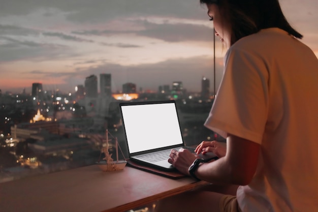 Mulher trabalhando com laptop perto do apartamento windows com vista da cidade à noite