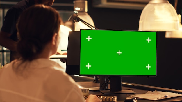 Mulher trabalhando com modelo de tela verde no computador, olhando para o fundo de maquete em branco. Analisando a tela com exibição de chroma key isolada na tela ao pôr do sol no escritório, empresa de inicialização.