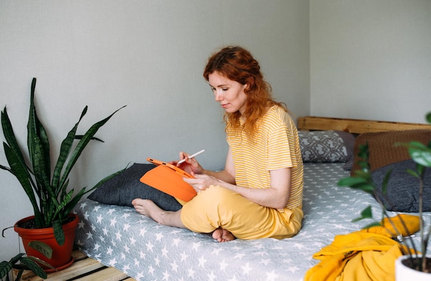 Mulher trabalhando em casa na cama usando tablet gráfico para design e desenho