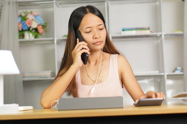 mulher trabalhando em casa Use seu telefone e computador para se comunicar com seus companheiros de equipe