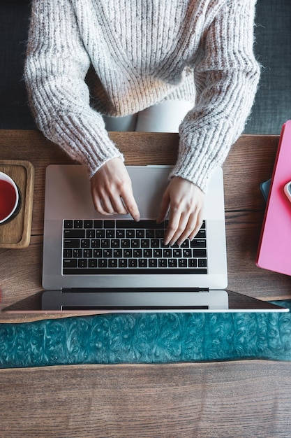 Mulher trabalhando em um laptop em um café com uma xícara de chá vista superior