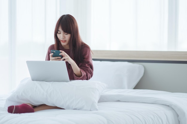 Mulher trabalhando em um laptop sentado na cama em casa.