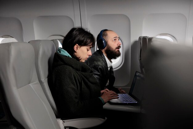 Mulher trabalhando no laptop durante o voo de avião no exterior, usando internet online no computador para viajar para o destino de férias. Turista esperando para chegar após a viagem de transporte de voo comercial.