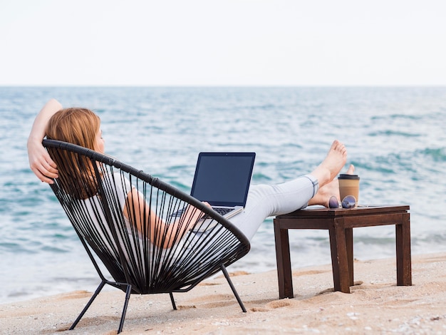 Mulher trabalhando no laptop na cadeira de praia