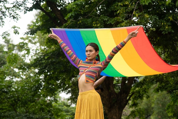 Mulher trans usando um vestido de arco-íris e segurando uma bandeira de arco-íris posa com confiança e orgulho de seu conceito de estilo de vida genderlgbtq mês do orgulho lgbtq